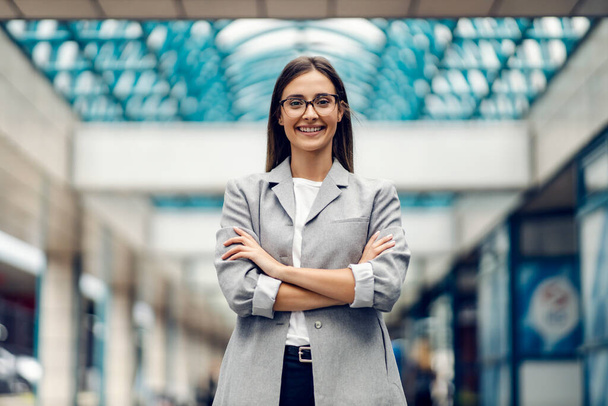Μια επιτυχημένη, ευτυχισμένη επιχειρηματίας, κομψά ντυμένη, να στέκεται στο επιχειρηματικό κέντρο με σταυρωμένα τα χέρια. Μια υπερήφανη, επιτυχημένη επιχειρηματίας στο επιχειρηματικό κέντρο - Φωτογραφία, εικόνα