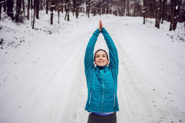 Sportswoman in warm outfit doing yoga exercises in snowy forrest. Fitness outdoors, snow, cold, nature fitness - Photo, Image