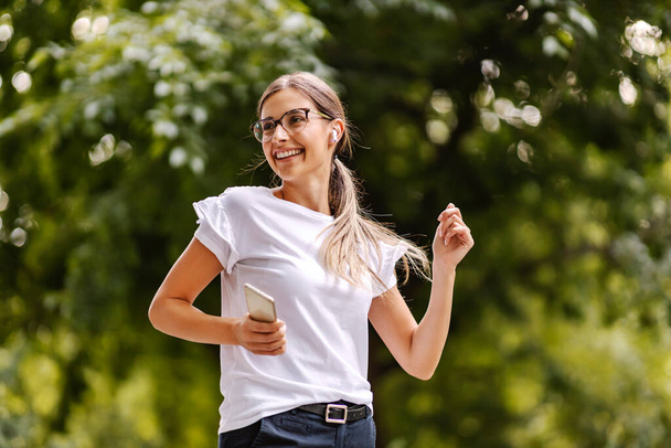 Una giovane donna felice che ascolta musica al telefono e balla nella natura. Una giornata nel parco - Foto, immagini