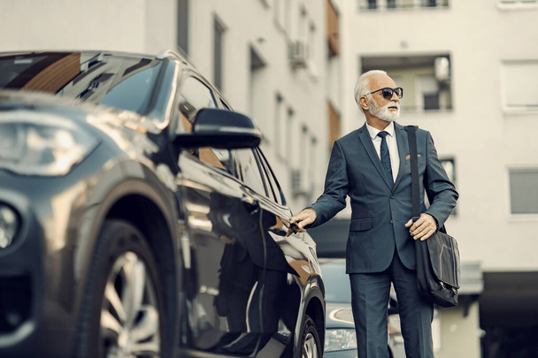 Un viejo hombre de negocios abriendo su coche. Un hombre de negocios mayor con un traje caro abriendo su coche y va a trabajar. - Foto, imagen