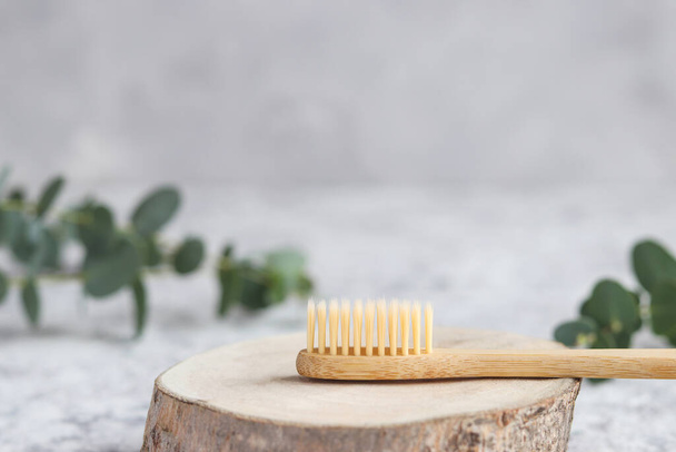 Eco-friendly bamboo toothbrush on a wood cut and eucalyptus leaf against grey wall with copy space. Oral hygiene and zero waste concept. Selective focus - Fotografie, Obrázek