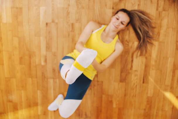 Спортсменка лежить на підлозі і розтягує силову гуму ногою. Вона робить фізичні вправи
. - Фото, зображення