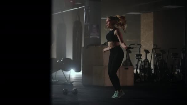 joven mujer deportiva está saltando la cuerda, saltando y calentando el cuerpo en el gimnasio antes del entrenamiento - Imágenes, Vídeo