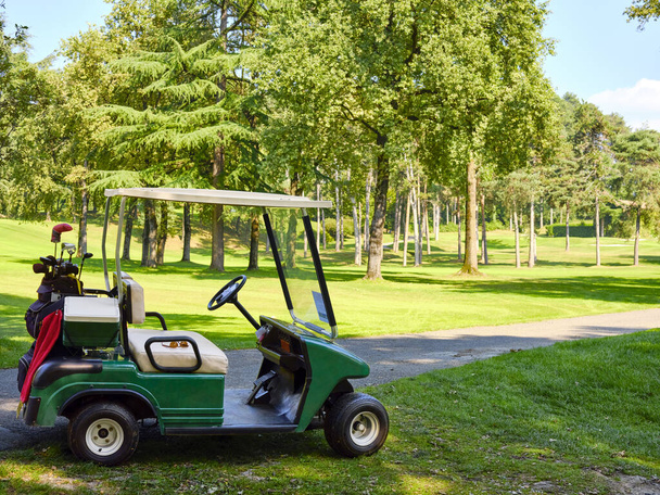 Samochód golfowy z torbą i kijami golfowymi na środku toru wodnego na polu golfowym. - Zdjęcie, obraz