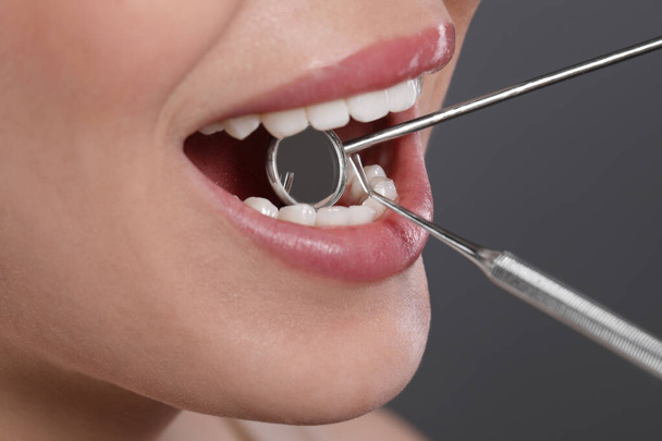 Examining woman's teeth with dentist's mirror on grey background, closeup - Fotografie, Obrázek