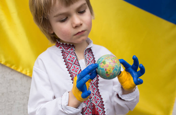 enfant en vêtements nationaux tient petit globe ballon. Les mains des enfants peintes en couleurs du drapeau ukrainien. arrêter la guerre en Ukraine. indépendance nationale. Enfants contre la guerre. Stand avec l'Ukraine - Photo, image