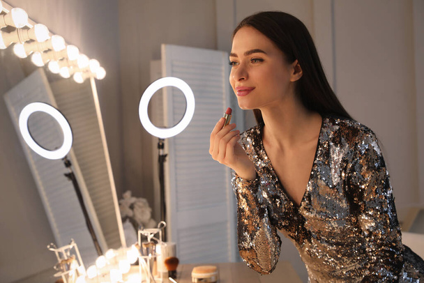 Young woman applying make up near illuminated mirror indoors - Фото, зображення