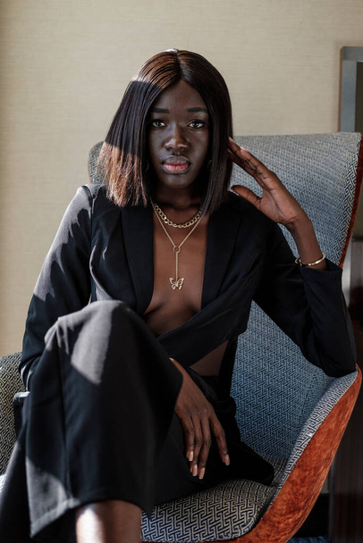 Portrait de jeune femme noire modèle. Elle porte un costume de femme d'affaires et elle est assise sur un siège. - Photo, image