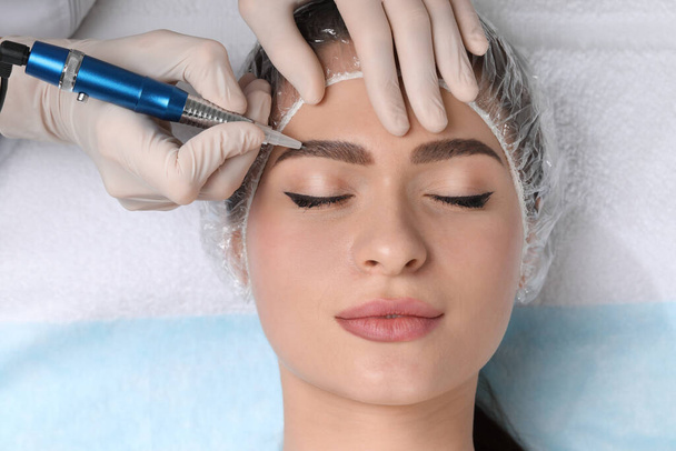 Young woman during procedure of permanent eyebrow makeup in beauty salon, closeup - Фото, изображение