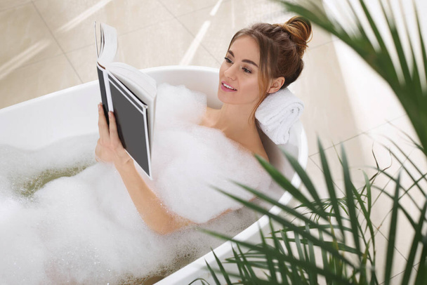 Beautiful woman reading book while enjoying bubble bath at home - Foto, afbeelding