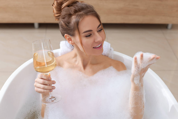 Beautiful woman with glass of wine enjoying bubble bath at home - Zdjęcie, obraz