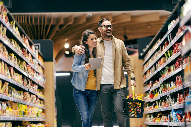 Усміхнена пара купує продукти зі списку в супермаркеті
. - Фото, зображення