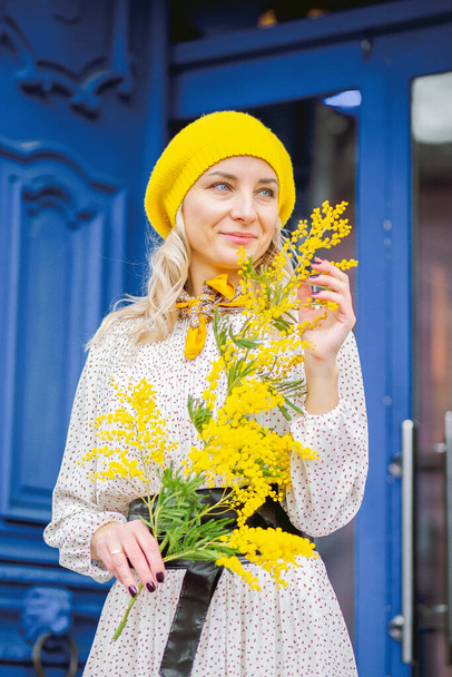 Portrait of a beautiful woman in a yellow beret with a sprig of mimosa on a spring day - Foto, Imagem