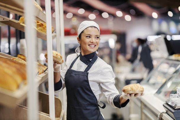 Bakery department seller in supermarket selling fresh buns at supermarket. - Photo, Image