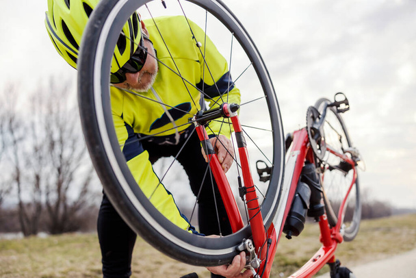 Vanha polkupyöräilijä tarkistaa polkupyörän puhjenneen renkaan. - Valokuva, kuva