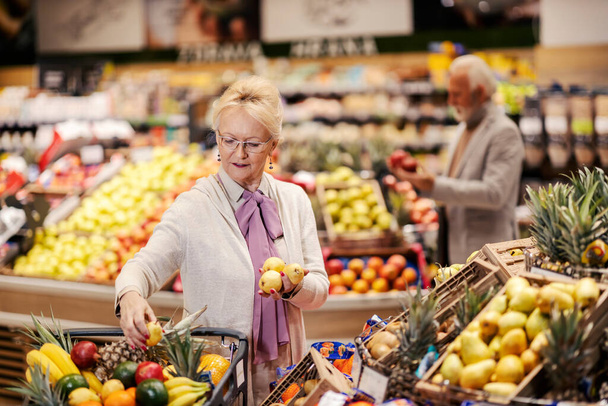Abuela poniendo frutas orgánicas en el carrito de la compra en el supermercado. - Foto, imagen