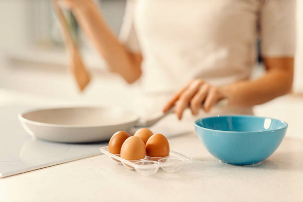 女性と一緒に朝食のためのキッチンカウンターで新鮮な卵バックグラウンドで朝食を作る. - 写真・画像