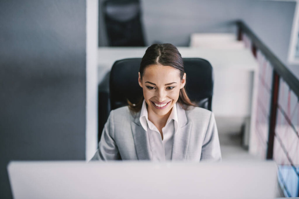 Самоотверженная улыбающаяся деловая женщина заканчивает доклад на компьютере в офисе. - Фото, изображение