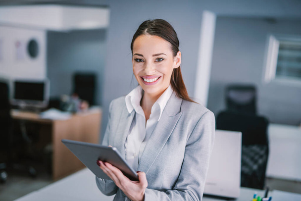 Una mujer de negocios sonriente trabajando en la tableta en la oficina. - Foto, imagen