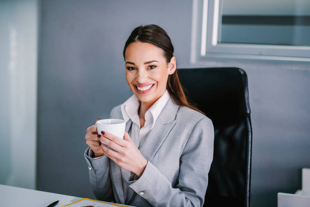 Portrait of a smiling businesswoman taking a coffee break at corporate firm. - 写真・画像