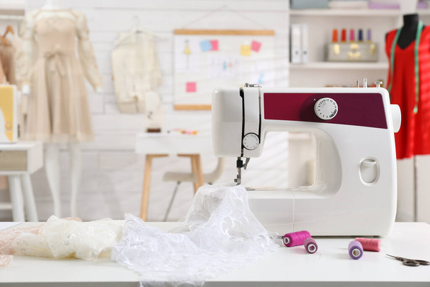 Modern sewing machine with fabric and bright threads on table in dressmaking workshop - Фото, зображення