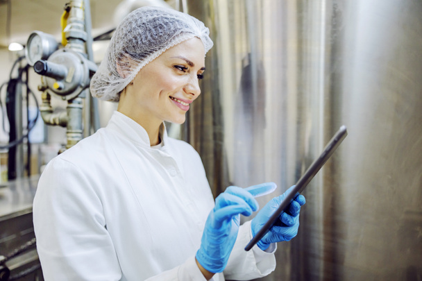 A female diary factory supervisor smiling at the tablet and scrolling on it. - Photo, Image