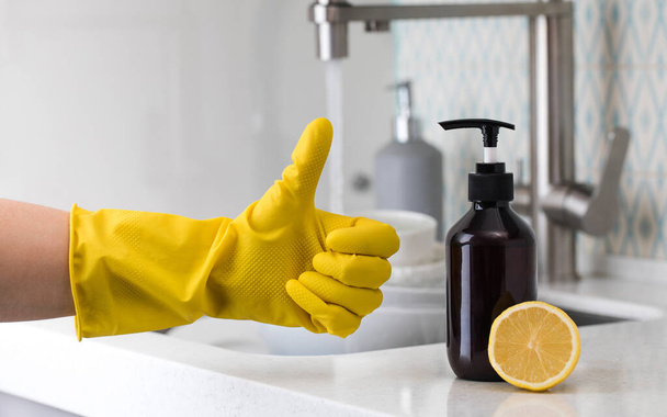 A bottle of eco-friendly dishwashing detergent with lemon and a yellow-gloved hand showing a thumbs up. - Foto, Imagen