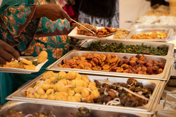 Nahaufnahme von afrikanischen Gerichten während eines Buffets auf einer Party. Gebratene Kochbananen, Kartoffeln, Fleisch und Gemüse - Foto, Bild
