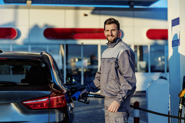 Een lachende benzinestation werknemer tanken auto tank met diesel. - Foto, afbeelding
