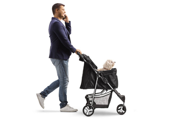 Full length profile shot of a man pushing a dog carriage and using a phone isolated on white background - Fotografie, Obrázek