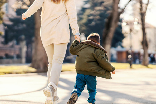 Achteraanzicht van moeder en jongetje hand in hand, rennen en spelen in een park. - Foto, afbeelding
