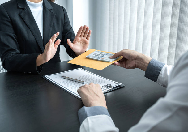 Business woman refusing and don't receive money banknote in envelope offer from business people to accept agreement contract of investment deal. - Photo, Image