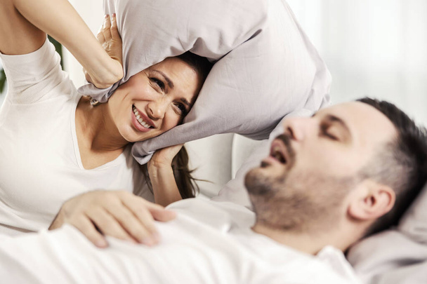 Жінка з подушкою, що закриває вуха через хропіння чоловіка
. - Фото, зображення