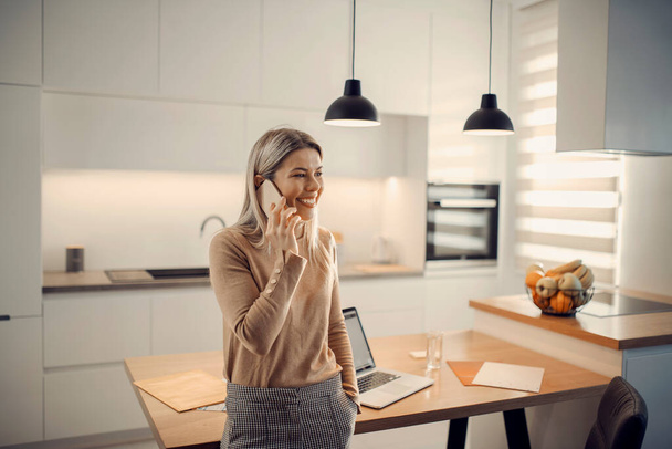 A happy entrepreneur having a phone call in kitchen at her home. - Photo, Image