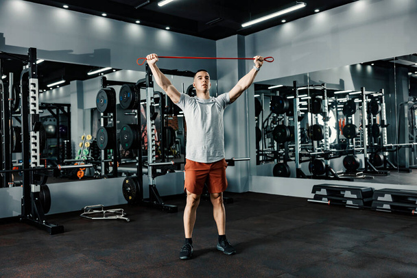 A sportsman doing fitness exercises with resistance band in a gym. - Photo, Image
