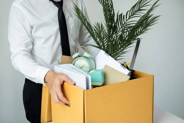 Zakenman werknemer stressvolle ontslag nemen uit het werk, terwijl het oppakken van persoonlijke bezittingen in bruine kartonnen doos en dragen om weg te lopen van kantoor - Foto, afbeelding