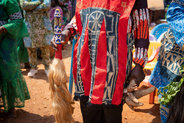 Primer plano del vestido africano usado por un caballero que sostiene una cola de caballo decorativa tradicional y un tubérculo durante una celebración africana - Foto, Imagen