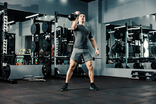 Un bodybuilder fort soulevant bouilloire-cloche avec un bras dans une salle de gym. Un exercice de musculation dans une salle de gym. - Photo, image