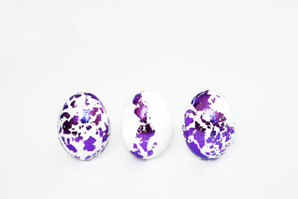 Three Easter eggs with pieces of decorated foil stand in a row on a white background. Religious holiday of Holy Easter - Photo, Image