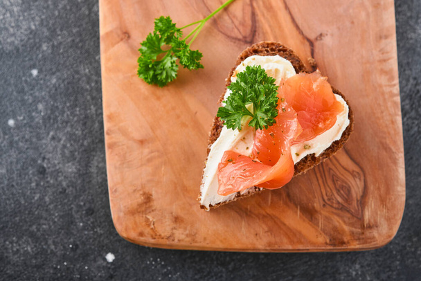 Mini sandwiches with salmon, curd cheese, parsley and rye bread in form of hearts. Valentine's day homemade creative food. Love breakfast design. Selective focus and copy space - Foto, imagen