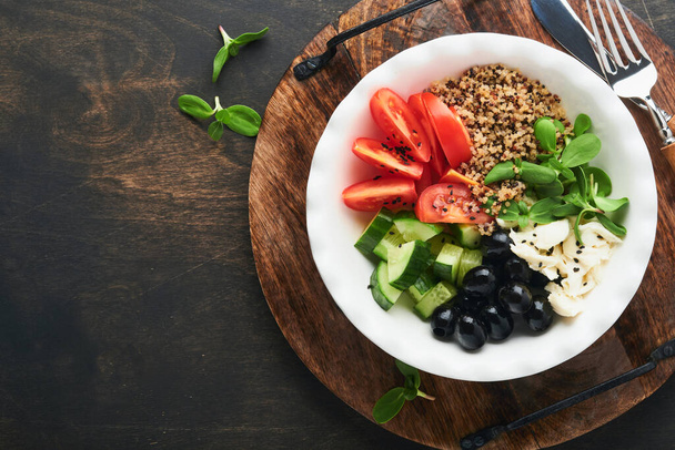Vegetarian Vegan salad bowl or buddha bowl with tomato, cucumber, mozzarella cheese, quinoa, olives and microgreens. Healthy and balanced food concept on old wooden dark background Top view copy space - Photo, Image
