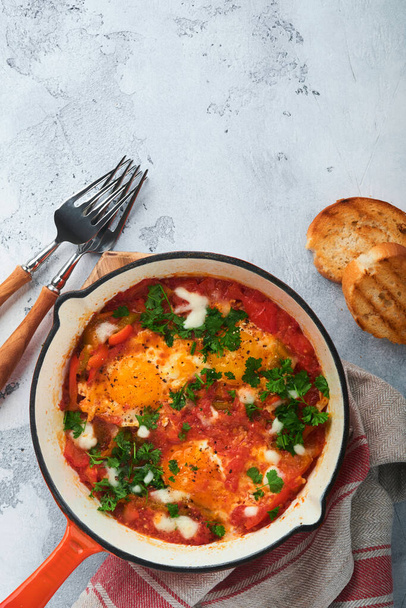 Shakshuka. Fried eggs with vegetables in iron frying pan on light grey slate, stone or concrete background. Traditional cuisine of Israel. Late breakfast concept. Top view, banner - Фото, зображення