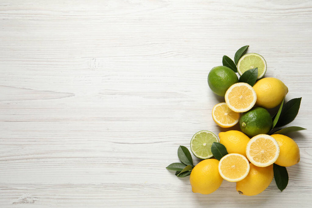 Fresh ripe lemons, limes and green leaves on white wooden background, flat lay. Space for text - Valokuva, kuva