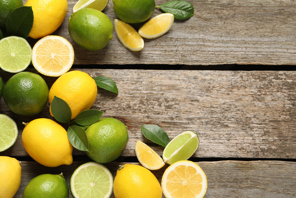 Świeże dojrzałe cytryny, limonki i zielone liście na drewnianym tle, płaskie leżaki. Miejsce na tekst - Zdjęcie, obraz