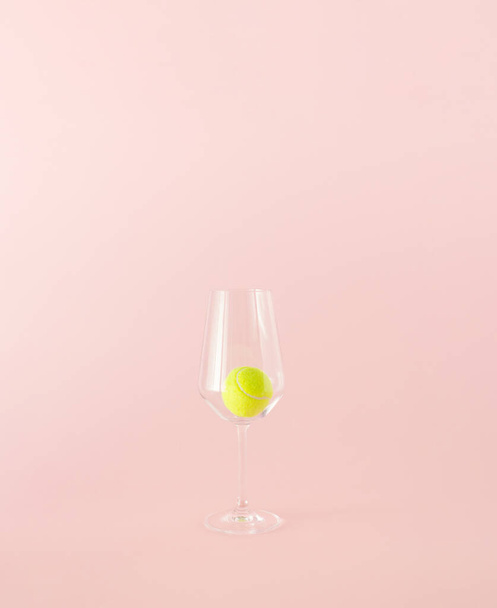 Жовтий тенісний м'яч у прозорому склянці для пиття на рожевому фоні. Мінімальна концепція
. - Фото, зображення