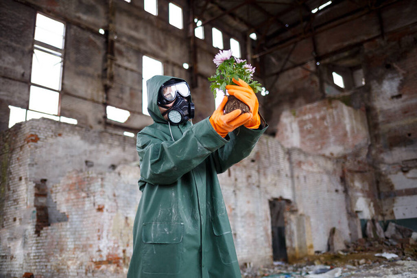 A dosimetrist scientist radiation inspector in protective clothing and a gas mask examines the danger zone. Close-up. Flower. Ecological catastrophy - Photo, Image