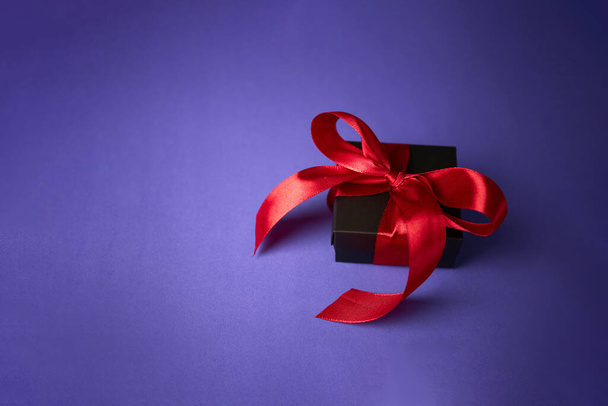 schwarzes Geschenk mit roter Schleife auf lila Hintergrund. Valentinstag. Geburtstag oder Feiertage Konzept. Kopierraum - Foto, Bild