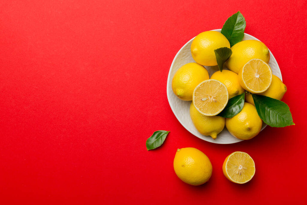 Taze kesilmiş limon ve tüm limonları renkli arka planda yuvarlak tabakta. Yemek ve içecek malzemeleri hazırlanıyor. Sağlıklı beslenme teması üst görünüm kopyalama alanı. - Fotoğraf, Görsel