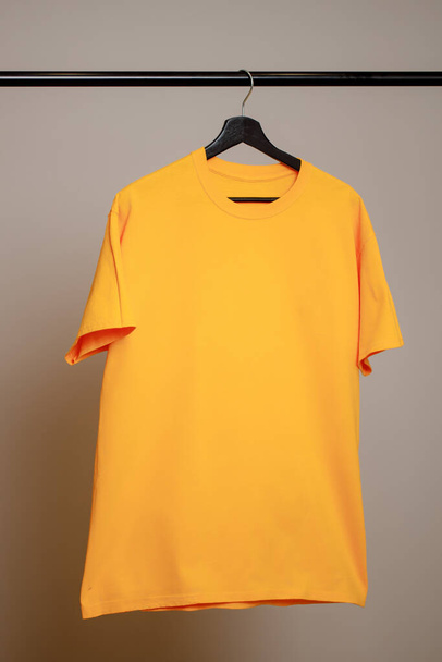 Pusty żółty T-shirt wiszący na wieszaku na szarym tle. Makieta do projektowania - Zdjęcie, obraz