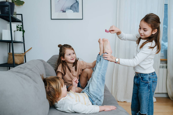 Experimenting girls tickling boy's feet with feather. He straightening his legs towards it, curious about the sensation. - Фото, изображение